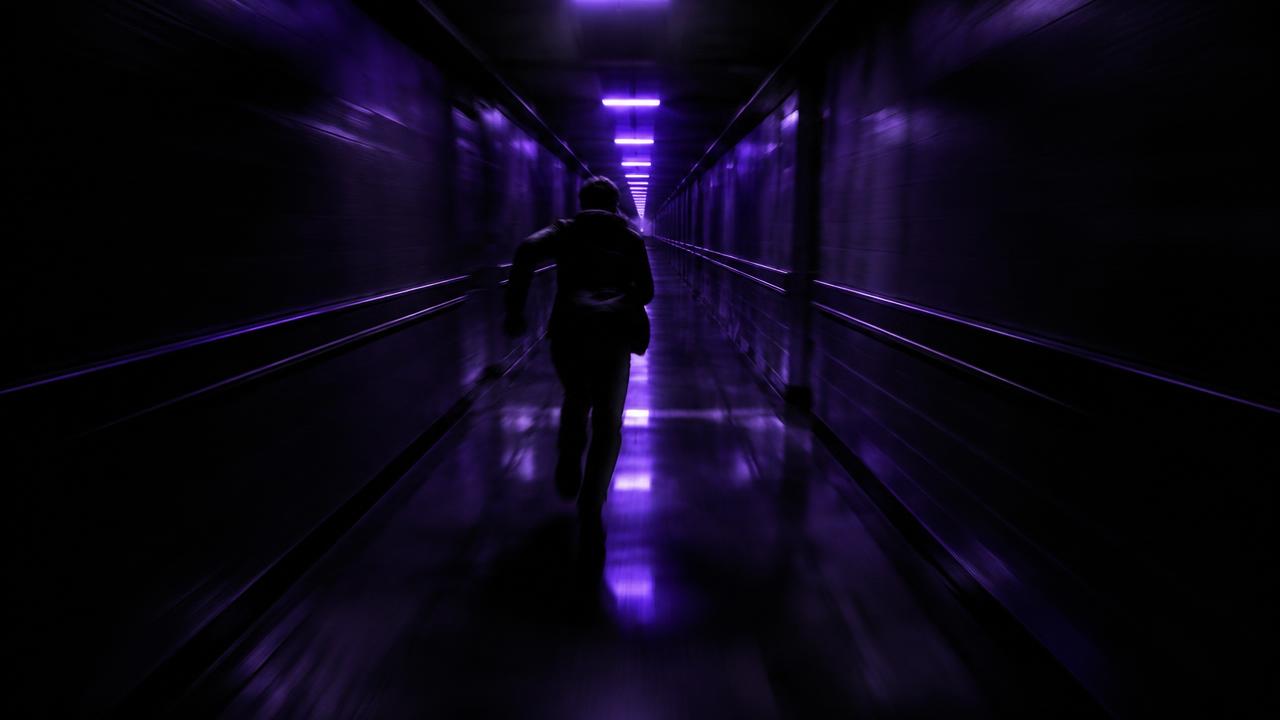 A figure running down an endless corridor lit by violet lights